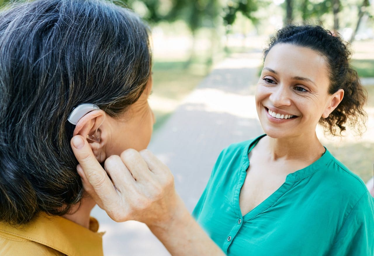 Woman using hearing aid while talking to her friend.