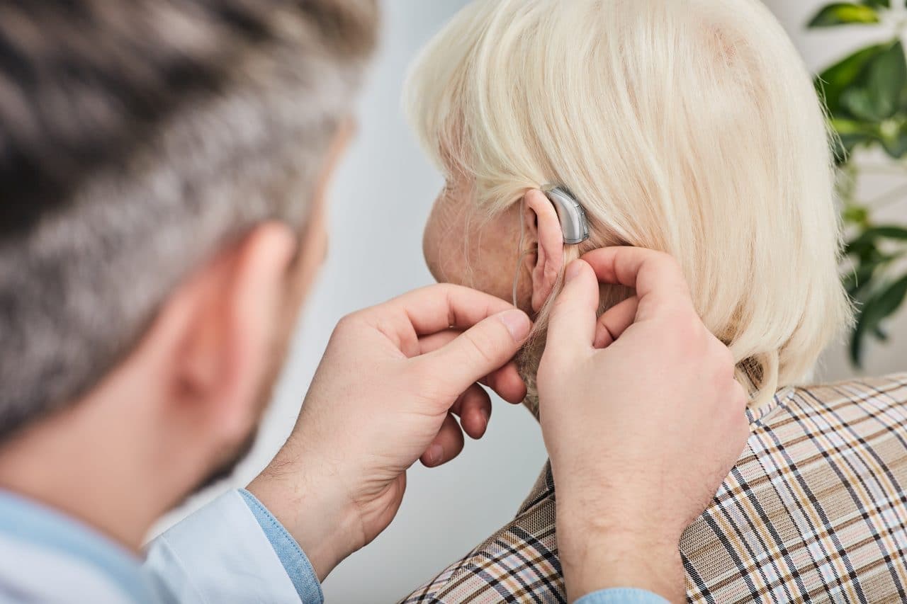 Audiologist fitting woman for hearing aids.