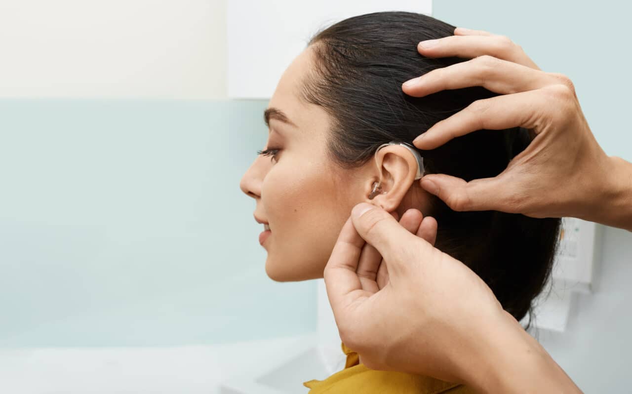 Installation hearing aid on woman's ear at hearing clinic, close-up, side view. Deafness treatment, hearing solutions
