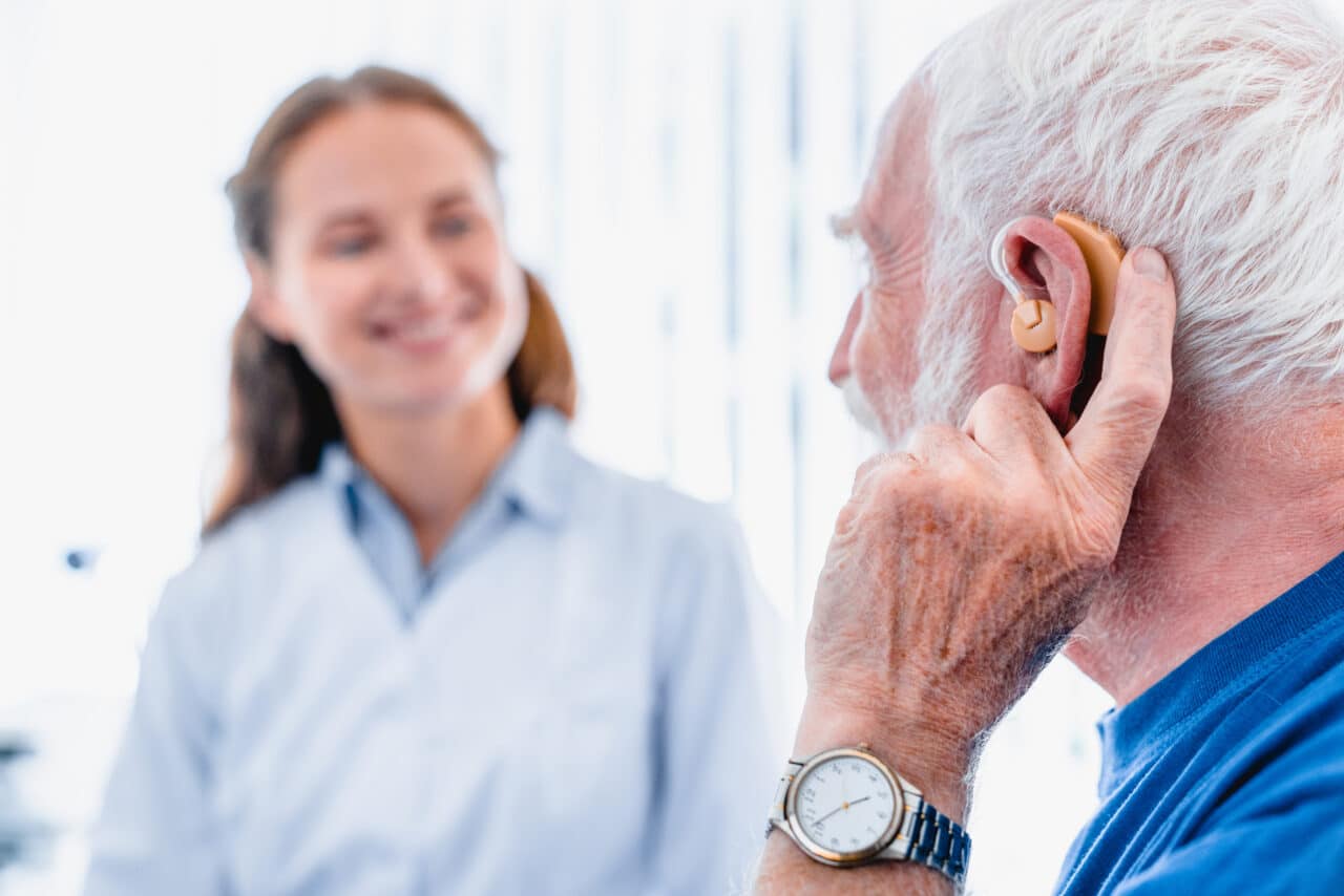 Older man with a hearing aid talking with his audiologist.