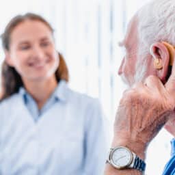 Older man with a hearing aid talking with his audiologist.