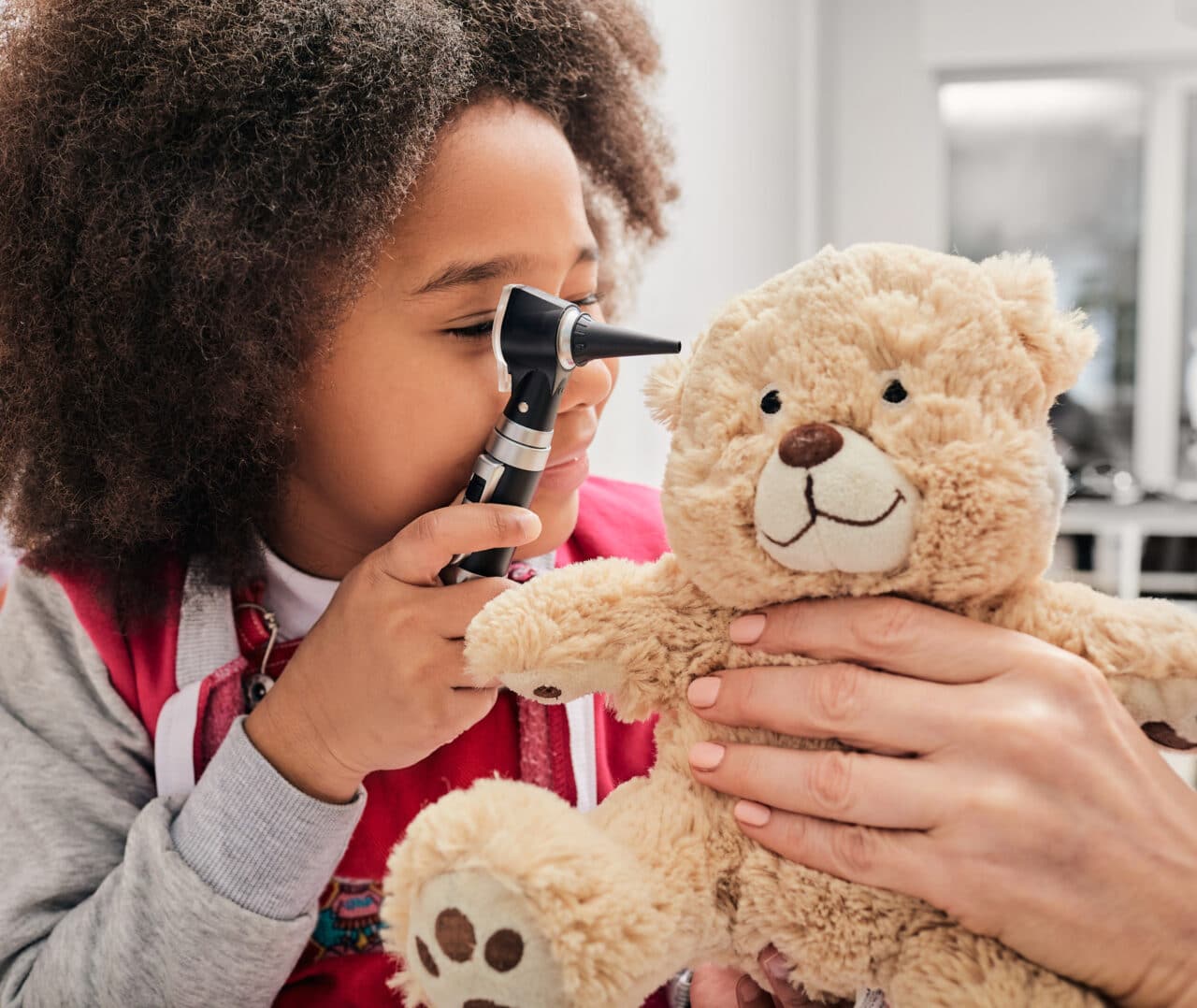 Girl plays with her toy bear in a medical game, using an otoscope. Hearing clinic for children