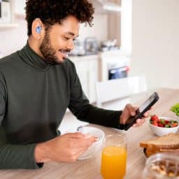 Smiling young man with hearing aids looking at his phone over breakfast.